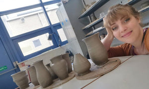 Tacha smiling in her pottery class next to pots