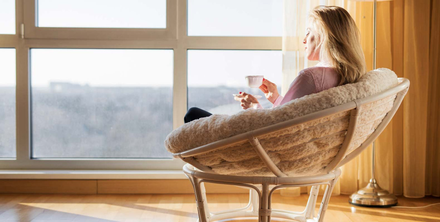 A lady sitting in front of a window holding a mug with her eyes closed