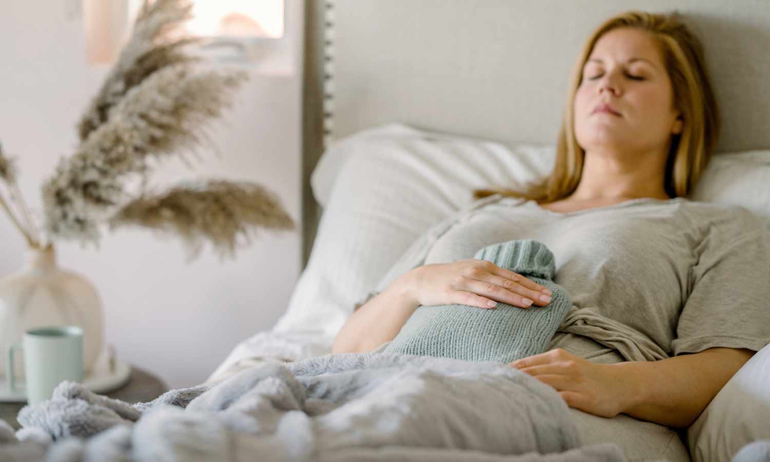 Lady suffering with IBS symptoms holding her tummy in pain with a hot water bottle