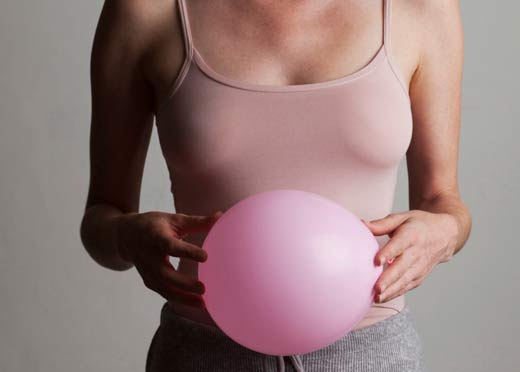 A lady holding a balloon next to her tummy showing how bloated she feels